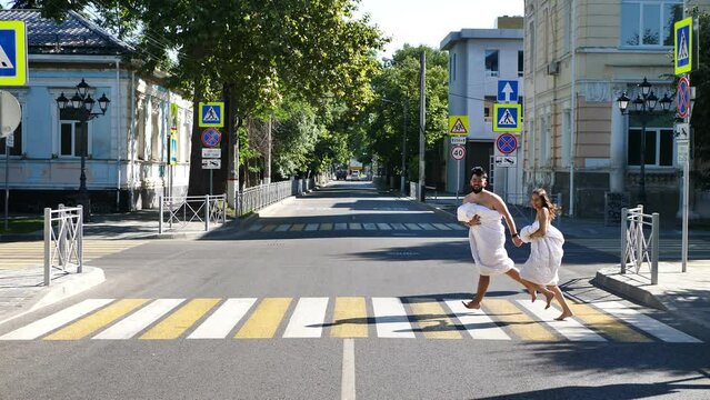 Young couple in love, a man and a woman, are running along the road in blankets at dawn.