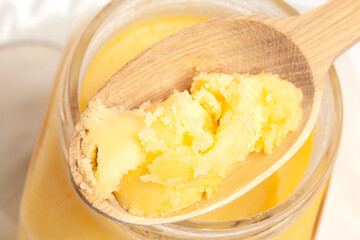 Ghee in jar and wooden spoon isolated on white background