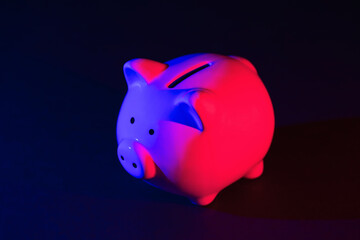 Piggy bank on a dark background with red-blue backlight. Banking concept. Bright neon lights on a...