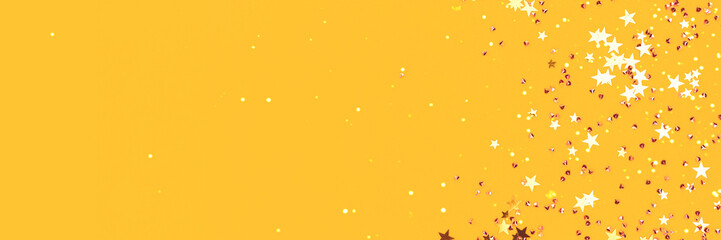 Golden stars and crystals confetti scattered on a yellow background. Festive concept with copy...