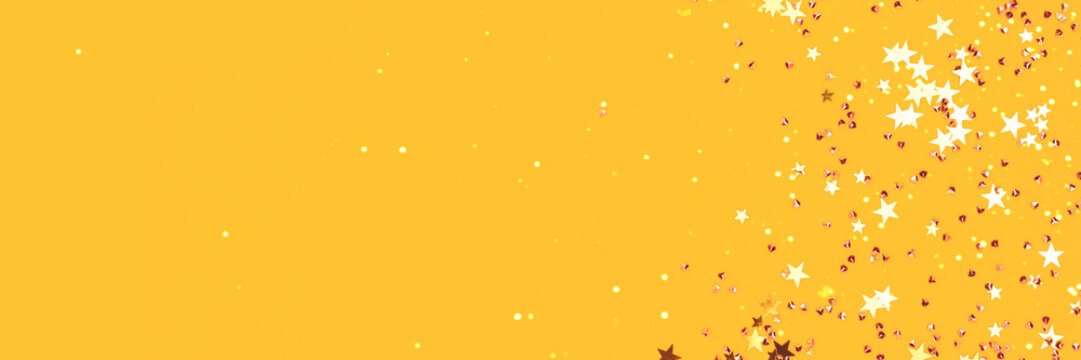 Golden stars and crystals confetti scattered on a yellow background. Festive concept with copy space. Selective focus.