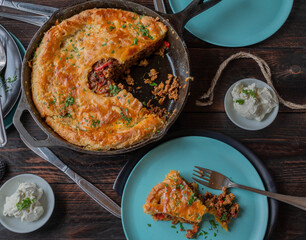 Savory pie with delicious ground beef, vegetables filling. Baked in a cast iron pan and served with plates on wooden table. Flat lay