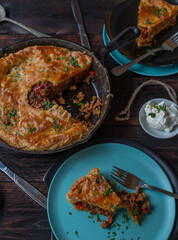 Meat pie with spicy ground beef, vegetable filling in a cast iron pan on wooden table 