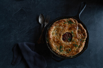 Savory pie in a cast iron pan on dark background with copy space.