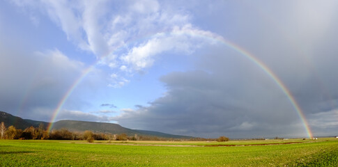 rainbow on dark rain clouds over green fields in the winter panorama