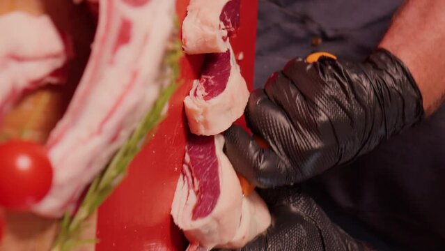 Vertical Screen: Butcher in gloves aggressively slicing raw lamb loin chops. Man hands cutting raw lamb meat for grill.