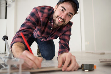 happy handyman holds a red pencil measuring a wooden plank