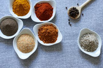 An assortment of spices in bowls for different dishes. Salt and spices, different types of peppers, turmeric and garlic.