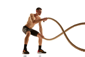 Portrait of muscular young man practicing with battle ropes during workout isolated over white...