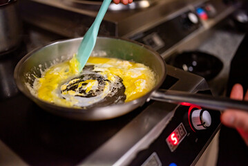 man chef cooking tasty scrambled eggs in frying pan on kitchen