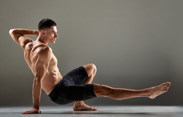 Portrait of male flexible muscular athlete showing animal flow sport elements isolated over gray...