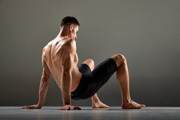 Fototapeta na wymiar Portrait of male flexible muscular athlete showing animal flow sport elements isolated over gray background. Fitness, trendy sports, beauty of body