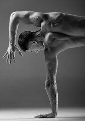 Cropped black and white footage of male muscular body doing hand stand isolated over gray background. Fitness, trendy sports, beauty of male body