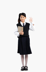 Asian junior schoolgirl in british international uniform standing full length holding book white background.
