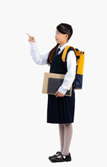 Back to school. Asian kid junior schoolgirl in uniform carrying backpack and books finger pointing standing full length white background.