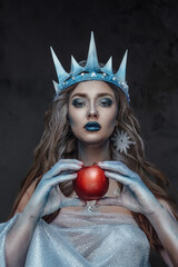 Portrait of attractive ice queen with red apple and frozen skin staring at camera.