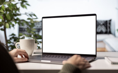 Fototapeta premium Modern laptop with blank white screen for copy replacement, woman using cozy home light interior with cup of steaming coffee