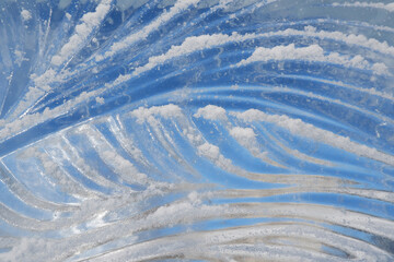 A textured fragment of a glacial wave-like pattern, sprinkled with white snow.A magical block of ice against the background of a winter blue sky.