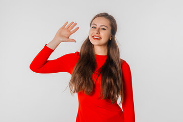 Friendly girl saying hi to best friends. Portrait of young girl with long hair in red dress, waving hand in hello gesture and smiling broadly, pleased to see familiar person