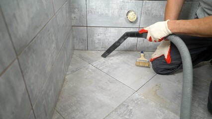 The worker removes the garbage with a vacuum cleaner. A worker vacuums the floor in a tiling...