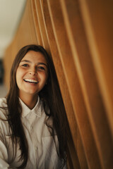 Girl standing at a wood background smiling with a white shirt
