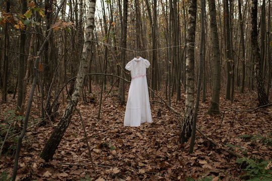 Lonely holy white communion or wedding dress hanging on wash line in forest in art concept