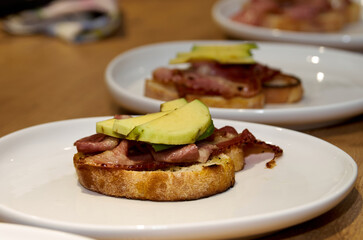 Toast with bacon and avocado on a plate standing on a wooden table