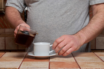 Fototapeta na wymiar Male hands pour coffee into a coffee cup standing on a tiled kitchen table