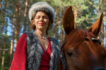 Fototapeta premium Woman in traditionsl clothes rides a horse in summer forest