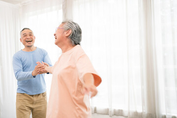 Romantic and cheerful Asian well-being senior couple enjoy dancing and holding hands to music together with smiles and happiness in the living room. Senior retirement activity at home.