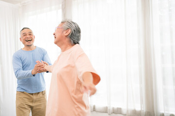 Obraz premium Romantic and cheerful Asian well-being senior couple enjoy dancing and holding hands to music together with smiles and happiness in the living room. Senior retirement activity at home.