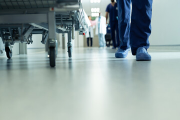 Fototapeta na wymiar Low section of legs of hospital workers walking and hospital bed in corridor, with copy space