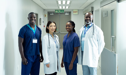 Portrait of diverse group of four doctors and healthcare workers smiling in hospital corridor