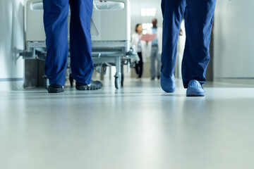 Low section of legs of hospital workers walking and hospital bed in corridor, with copy space