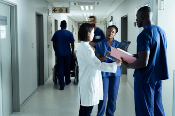 Diverse female doctor and healthcare workers discussing in hospital corridor, copy space