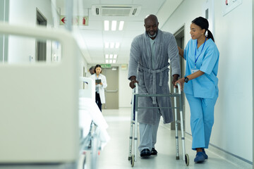 Diverse female healthcare worker helping senior african american male patient use in hospital