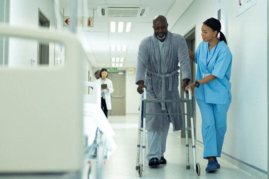 Diverse Female Healthcare Worker Helping Senior African American Male Patient Use In Hospital