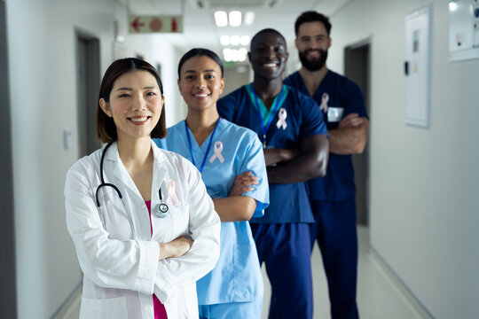 Portrait Of Diverse Group Of Smiling Healthcare Workers Wearing Cancer Ribbons Standing In Corridor