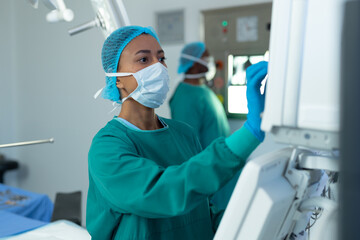 Biracial female surgeon operating computerised medical equipment in operating theatre