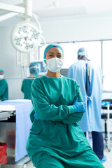 Vertical portrait of smiling biracial female surgeon in mask in operating theatre, with copy space