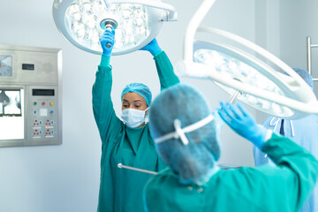 Biracial female surgeon and colleague adjusting lights in operating theatre for operation