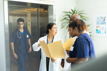 Diverse group of male and female doctors holding files discussing in busy hospital corridor