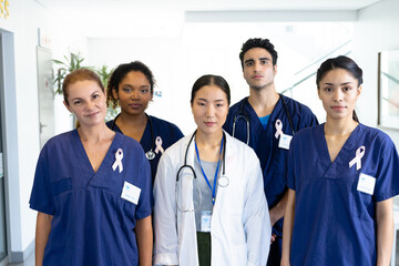 Portrait of diverse group of healthcare workers wearing cancer ribbons standing in hospital corridor