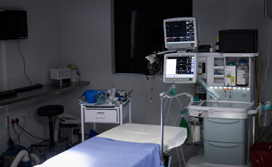 Electronic medical equipment with monitor screens on and empty operating table in operating theatre