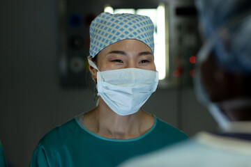 Female asian surgeon smiling to colleague in operating theatre during operation