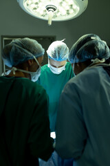 Vertical of diverse group of surgeons operating on patient in operating theatre, with copy space