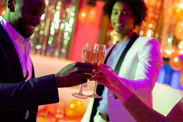 Three happy, diverse male and female friends making a toast with glasses of champagne at nightclub