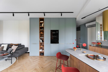 Interior design of colorful open space with built-in oven, bookcase, modern red hockers, wooden...