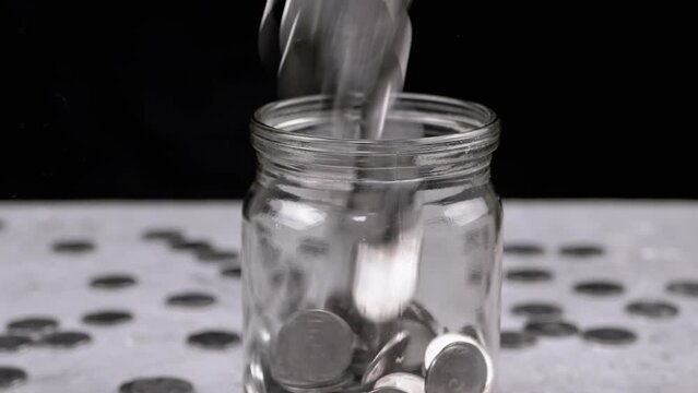 Silver Coins Fall into a Glass Jar against the Background of Scattered Kopecks. Time-lapse. Stream of Ukrainian cents pours. Piggy bank. Financial crisis, budget savings, money accumulation. Poverty.