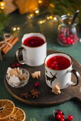 Spicy cranberry tea in two white mugs on a wooden board on a concrete green background in Christmas style. Merry Christmas concept.